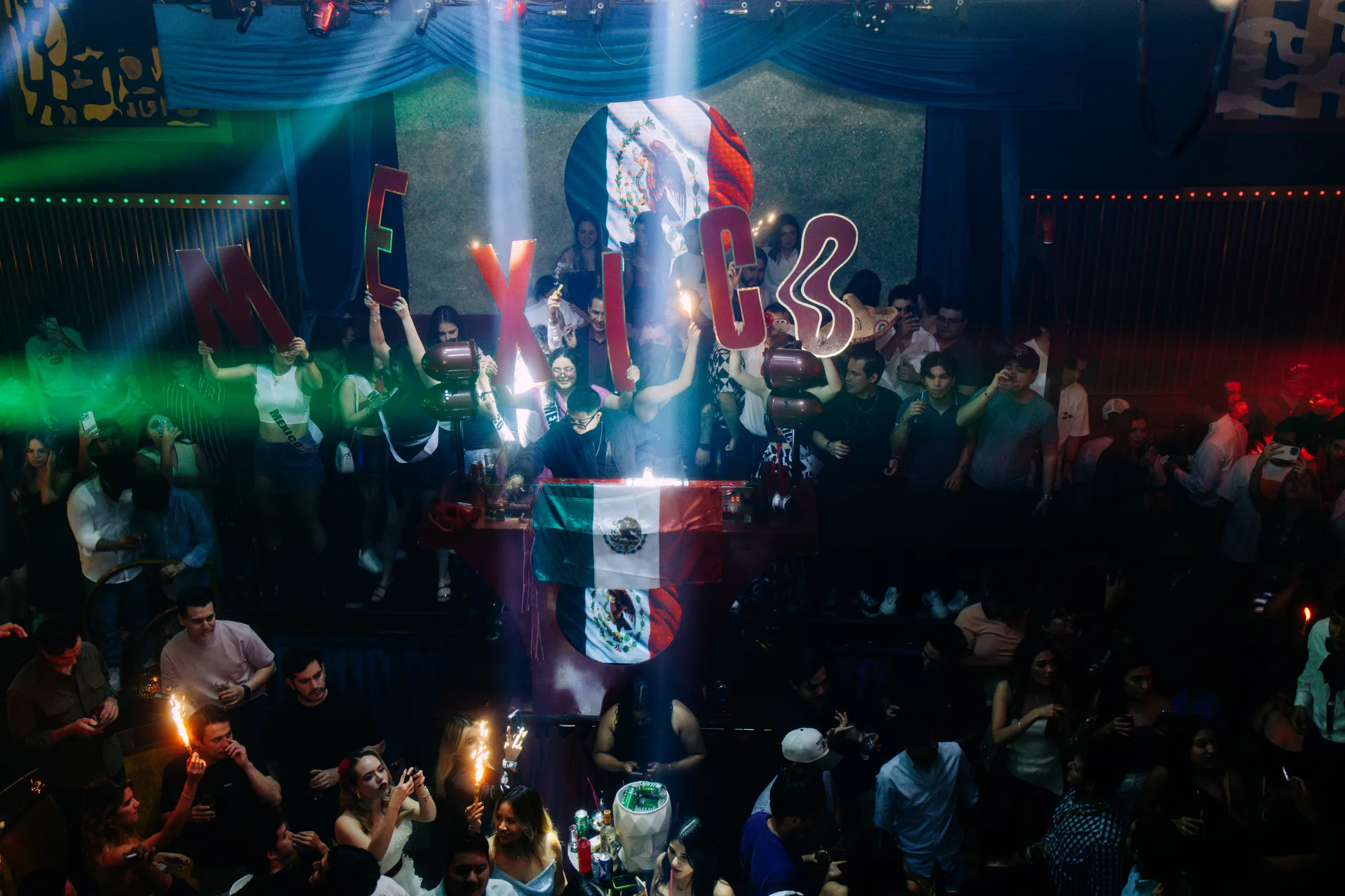 Pista llena en un festival con la bandera de México proyectada al fondo